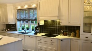 A kitchen with white cabinets, a black backsplash, and a window with a lace curtain. - Charming House with a Fantastic View of Norway's Nature (Ørsta)