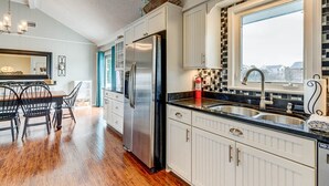 Een moderne keuken met witte kastjes, een roestvrijstalen koelkast, een zwart aanrecht en een raam met uitzicht.