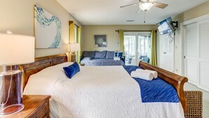 Een slaapkamer met een groot bed, een plafondventilator, een aan de muur bevestigde televisie en een raam met gordijnen.