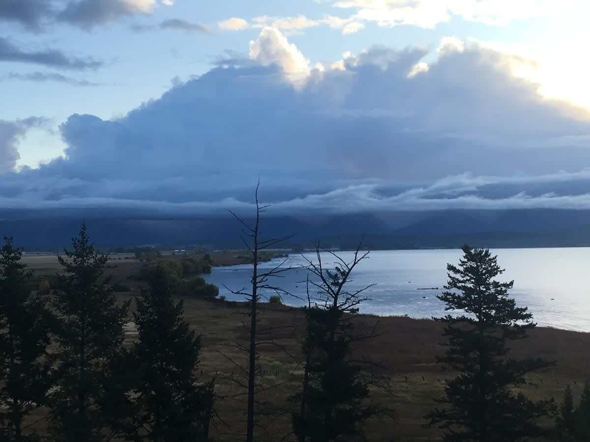 Un paysage comprenant une étendue d’eau, des arbres et un ciel nuageux.