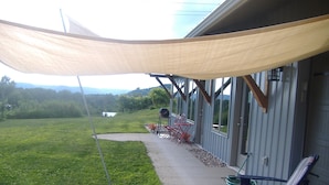 Un patio cubierto con mobiliario exterior, una parrilla de barbacoa y vistas a un campo de césped y montañas distantes.