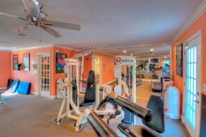 A home gym with exercise equipment, a ceiling fan, and a door leading to another room.