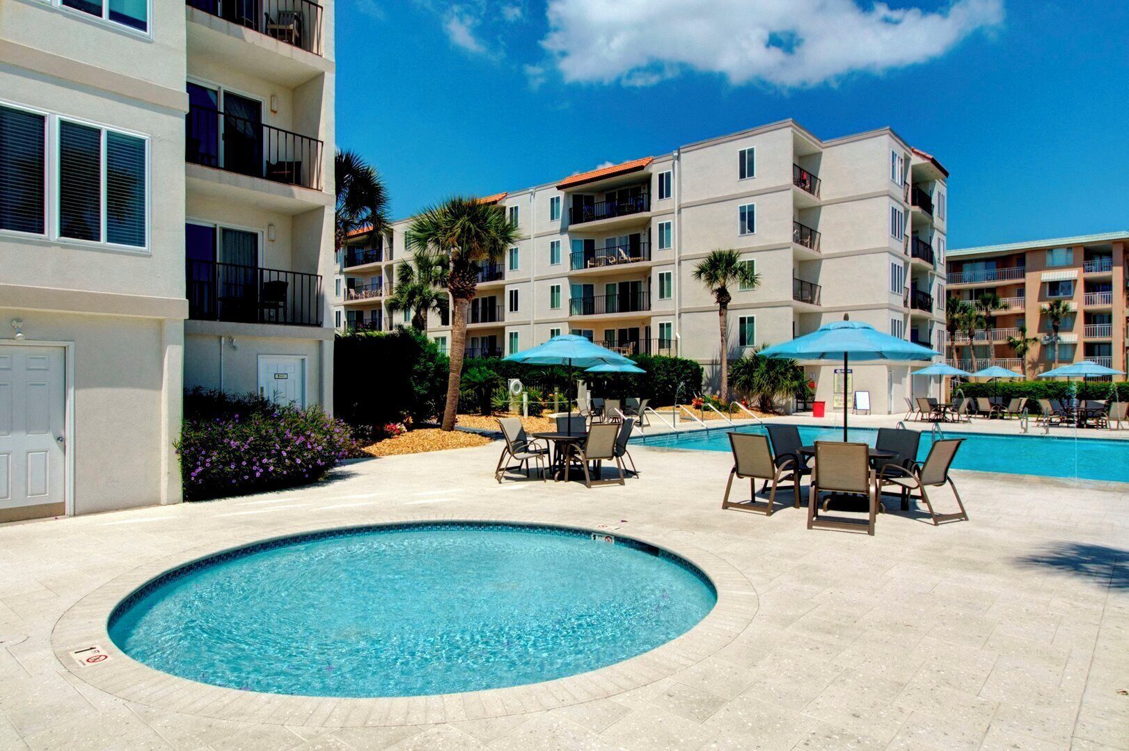 A swimming pool with lounge chairs and umbrellas, surrounded by multi-story buildings with balconies.