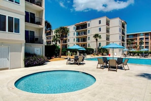 A swimming pool with lounge chairs and umbrellas, surrounded by multi-story buildings with balconies.