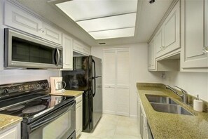 A modern kitchen with white cabinetry, a stainless steel refrigerator, a microwave, an oven, a coffee maker, and a granite countertop.
