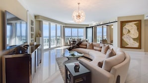 A spacious living room with a large sectional sofa, a glass coffee table, and a modern chandelier.