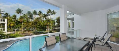 A balcony with a glass railing, a pool, and a table with chairs.