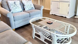 Un salon avec un canapé gris, une table basse en osier blanche et un meuble blanc.