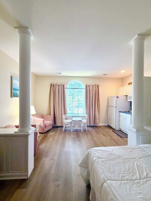Une chambre d’hôtel comprenant un lit, une petite table à manger, une chaise, un coin cuisine et une fenêtre avec des rideaux.