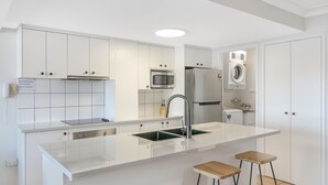 Ett modernt kök med vita skåp, en diskho i rostfritt stål, en mikrovågsugn, ett kylskåp och en inbyggd tvättmaskin.