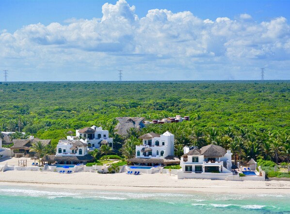 A coastal resort with multiple white buildings, some with thatched roofs, and a beach in the foreground. - Secluded Beach Front Boutique Resort with 6 Villas, each with Private Pools! (Playa del Carmen)