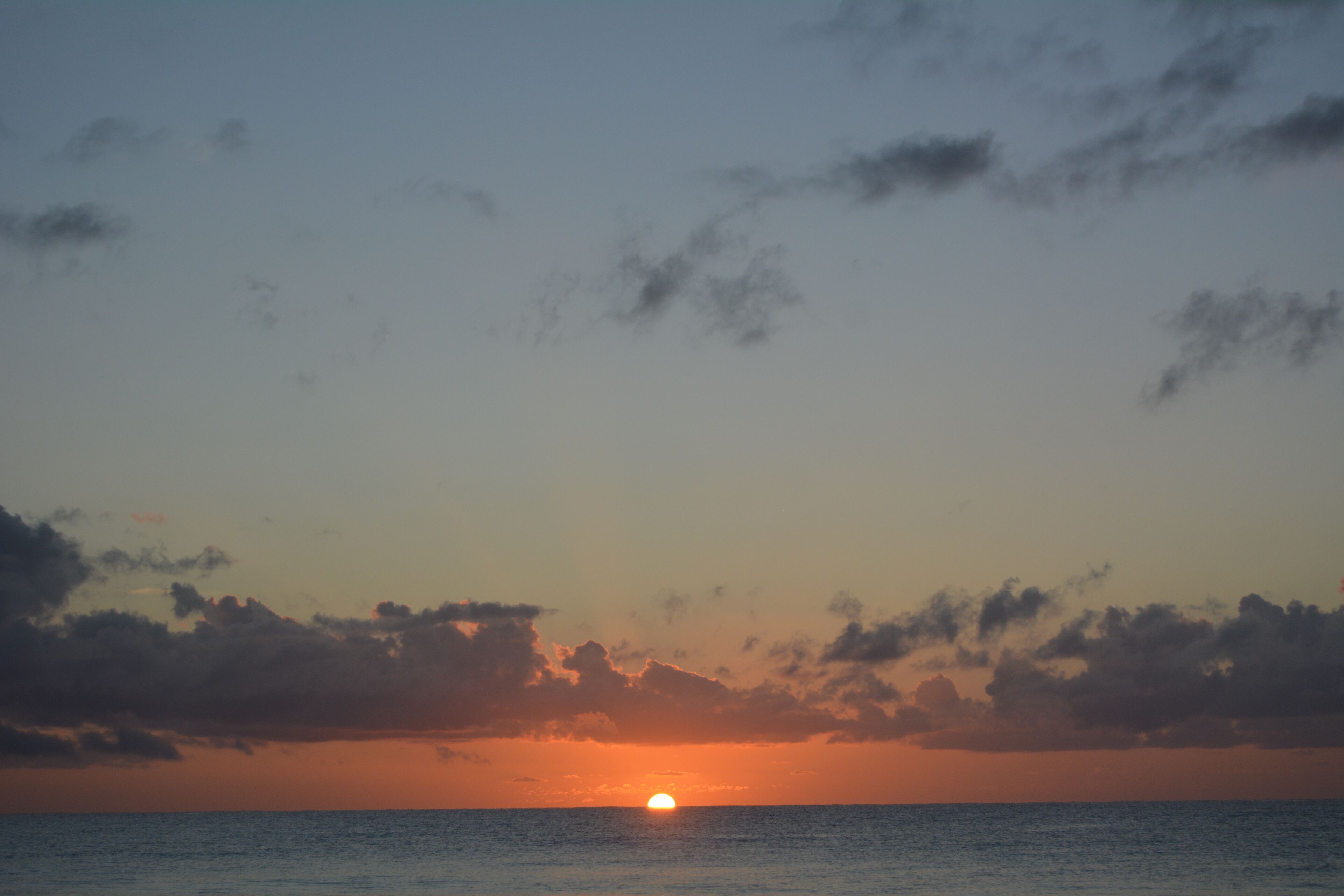 A sunset over the ocean with clouds in the sky.