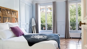A bedroom with a large bed, a wooden herringbone floor, a ceiling medallion, and a window with a view of greenery. - CAVALIER DES LIONS 2bedr 2 1/2baths (Paris)
