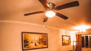 Ein Essbereich mit einem Glastisch, dunklen Stühlen, einem Deckenventilator und zwei gerahmten Bildern an der Wand.