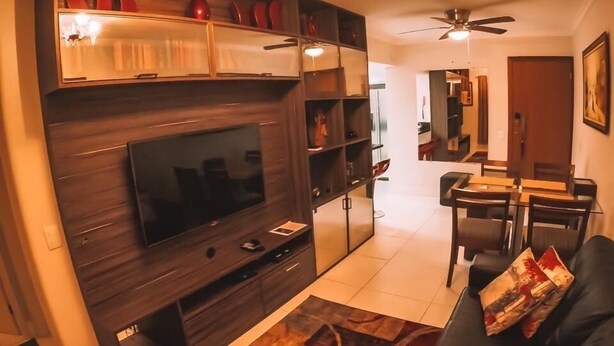 Ein modernes Wohnzimmer mit Flachbildfernseher, dunklen Holzregalen, einer schwarzen Ledersofa und einem gemusterten Teppich.