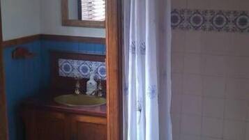 Un baño con tocador de madera, un espejo y cortina de ducha.