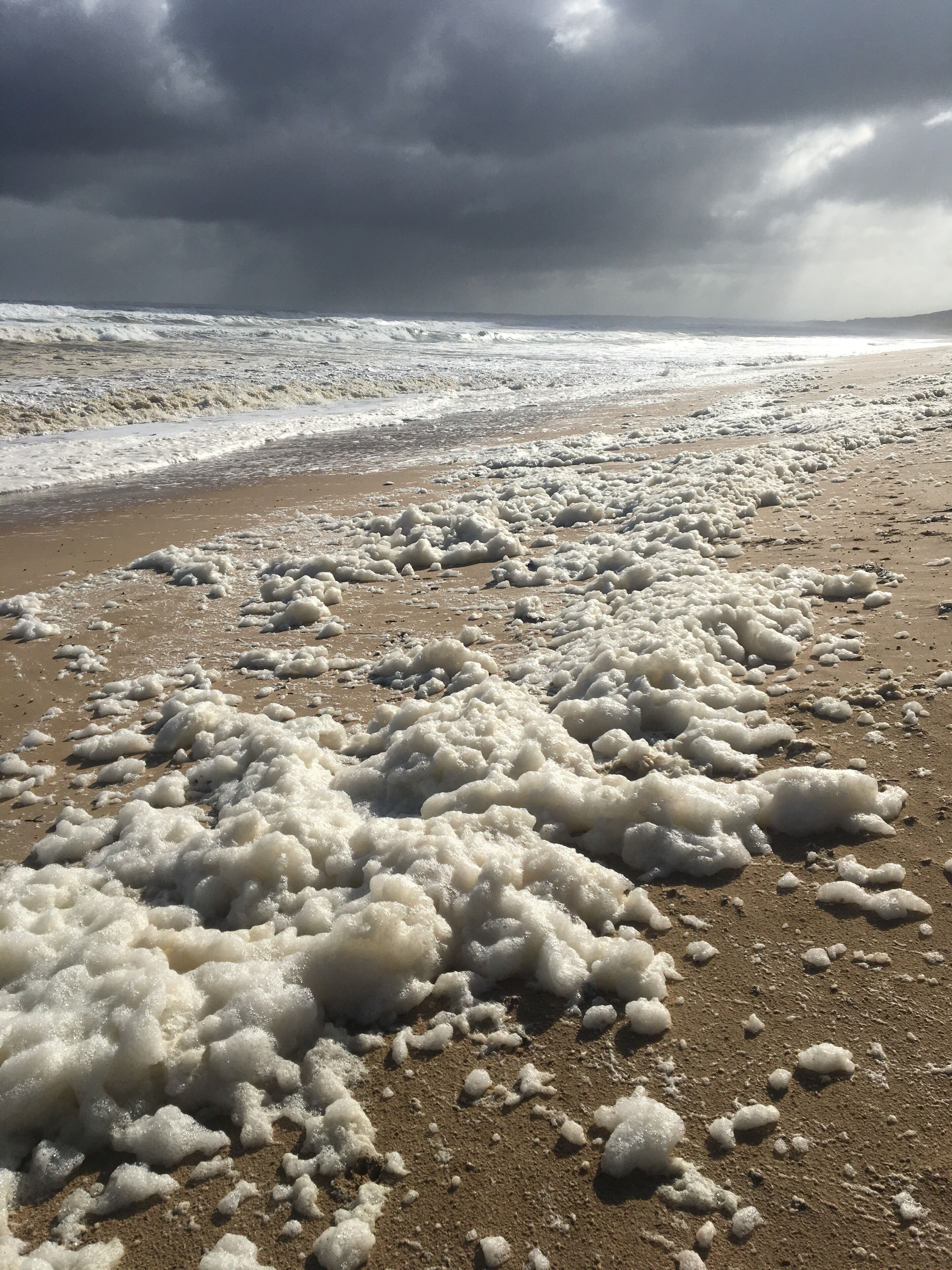 Een strand met schuimende golven en een bewolkte lucht.