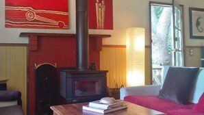 A cozy living room with a fireplace, a red couch, a wooden coffee table, and artwork on the walls. - Lavender Cottage Venus Bay (Venus Bay)