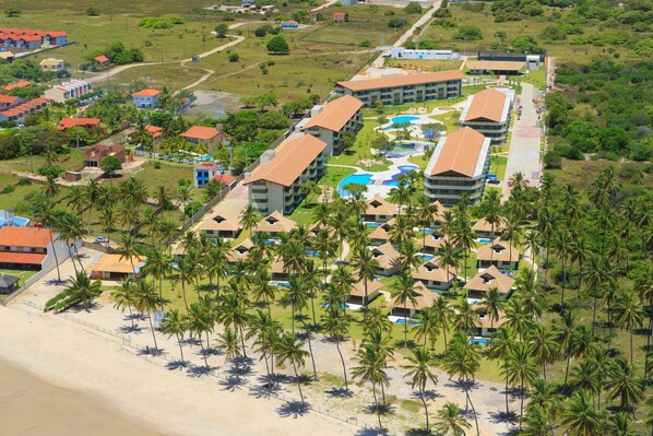 Ein Resort mit mehreren Gebäuden, einem Poolbereich und einem Strand mit Palmen.