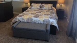 Un dormitorio con una cama, dos mesitas de noche, una banqueta y una ventana con persianas.