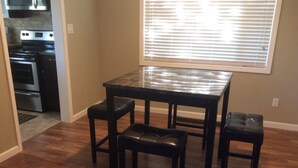 Una cocina con una mesa de madera oscura y cuatro taburetes, una ventana con persianas y suelo de madera.