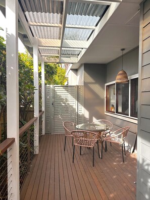 Une terrasse couverte avec un toit en verre, une table ronde en verre et des chaises en osier.
