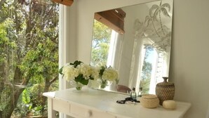 Un tocador blanco con espejo, un jarrón de flores blancas y objetos decorativos.