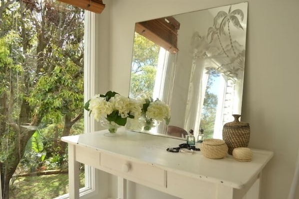 A white vanity with a mirror, a vase of white flowers, and decorative items.