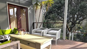 Una terraza con mesa de billar, dos sillas de mimbre blanco y un sofá con cojines verdes.