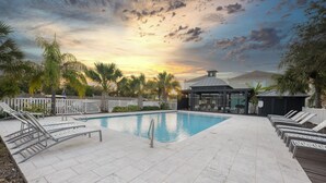 A swimming pool with lounge chairs, a gazebo, and a white fence.