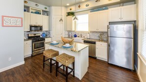 A kitchen with white cabinets, stainless steel appliances, a central island with stools, and decorative fish wall art.