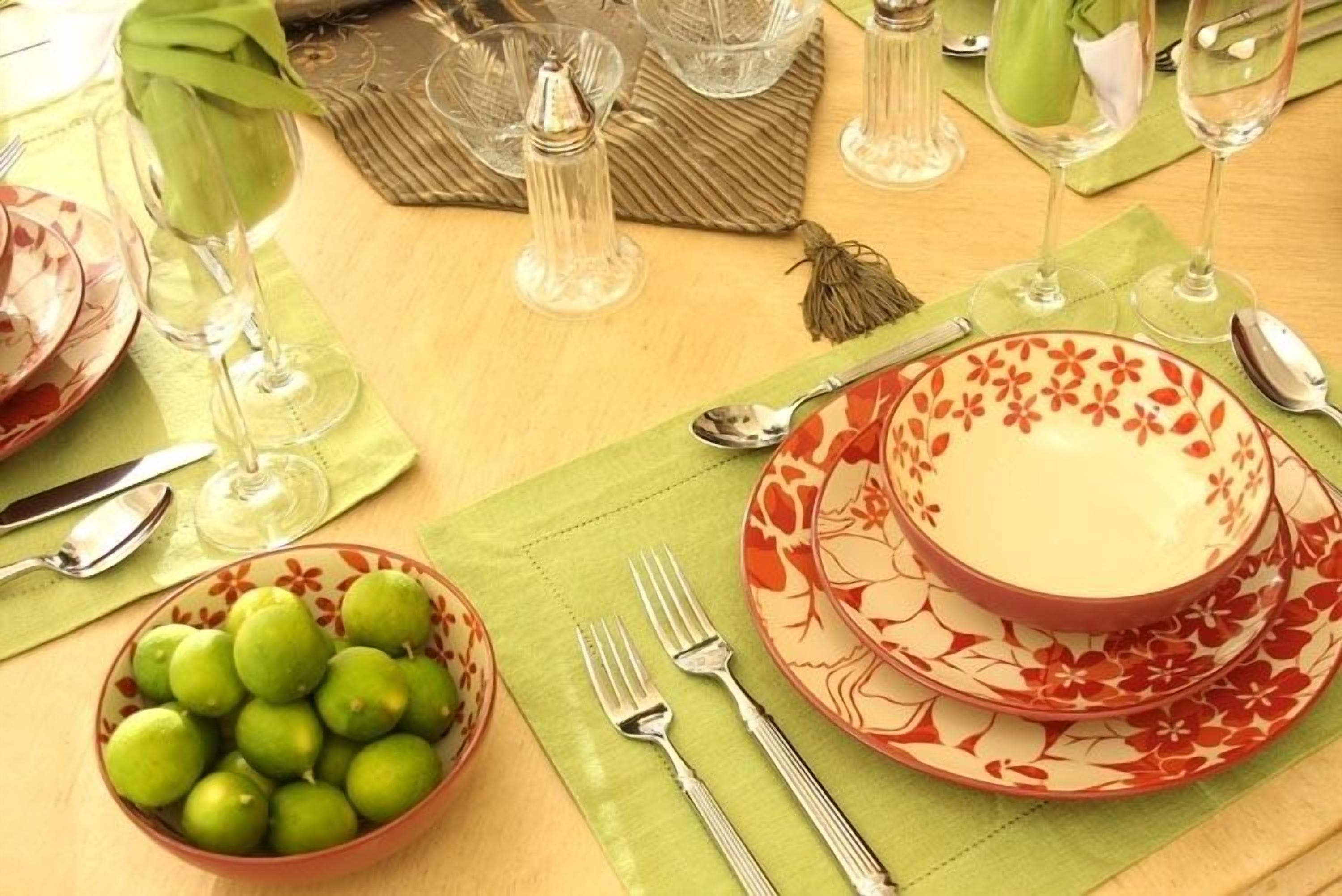 A table set for a meal with a bowl of green fruit, a red and white floral plate, and a clear glass.