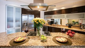 A modern kitchen with granite countertops, stainless steel appliances, and a central island with a vase of flowers and fruit. - Panoramic Oceanview, Luxury Condo 3 bd, 3bath on the beach. (Puerto Vallarta)