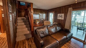 A wooden interior with a leather sofa, a staircase, and a view of the outdoors. - Chechessee River House (Okatie)