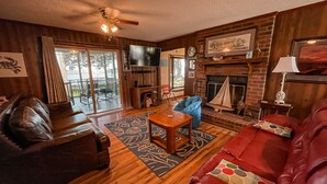 A cozy living room with a fireplace, leather sofas, a TV, and a ceiling fan. - Chechessee River House (Okatie)