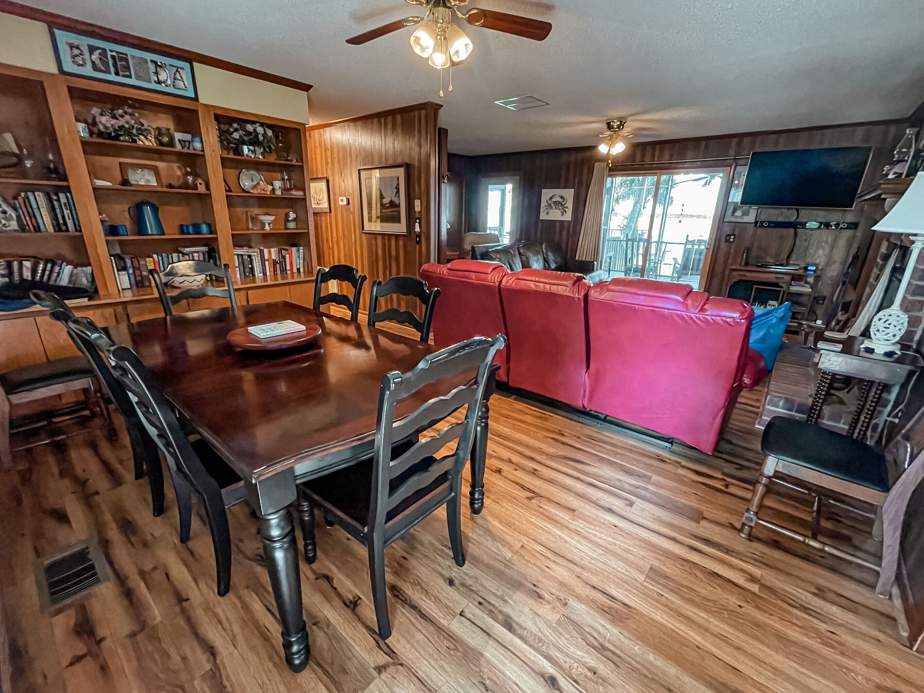 A spacious living room with a wooden dining table, red leather sofa, and a television.