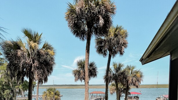 A wooden deck with a railing, overlooking a body of water with boats and a dock. - Chechessee River House (Okatie)