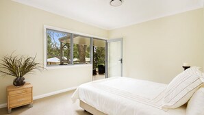 A bedroom with a bed, a nightstand, a potted plant, a window, and a door.