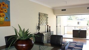A modern living room with a glass coffee table, a dark brown vase with a plant, a sofa, and a decorative wall piece.