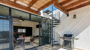 Un patio exterior moderno con puerta de vidrio que da a una sala de estar, una escalera en espiral y una parrilla para barbacoa.