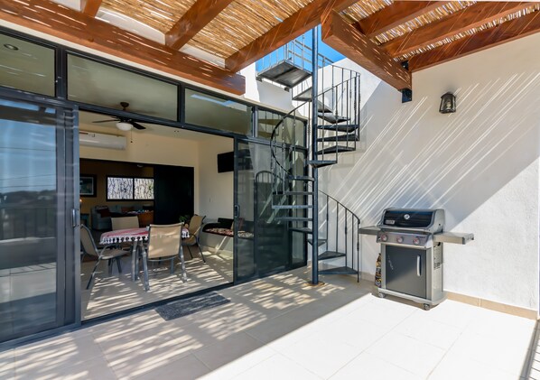 A modern outdoor patio with a glass door leading to a living area, a spiral staircase, and a barbecue grill. - Perfect House with Amazing View of the Ocean and 5 minute walk to the Beach! (San Jose del Cabo)
