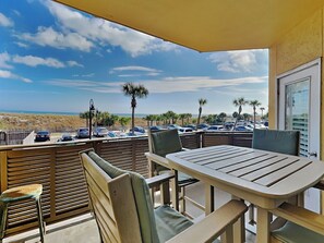 Een balkon met een tafel en stoelen, uitkijkend op een parkeerplaats en strand.