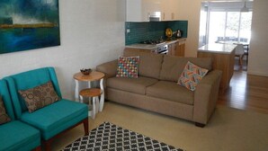 A living room with a sofa, coffee table, and a painting on the wall. - Dare St Beach Apartment | 2-Min Walk to Beach & Town (Ocean Grove)