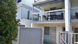 A modern two-story building with a balcony on the upper floor, a covered outdoor seating area, and a fenced patio. - Dare St Beach Apartment | 2-Min Walk to Beach & Town (Ocean Grove)