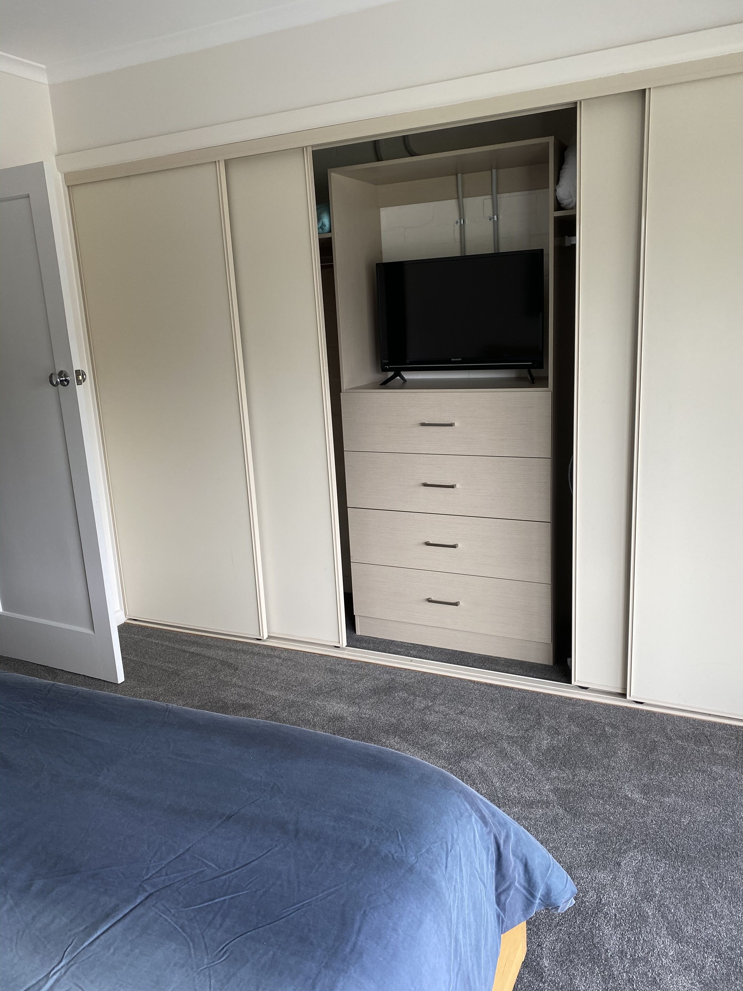 A bedroom with a bed, a wardrobe with a television on top, and a set of drawers.
