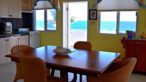 A kitchen with a dining table, chairs, and a view of the ocean. - Seaside Splendor:  2-3 BR w/ Expansive Deck, Panoramic Views, AC, Wifi, & Pool (Sandy Hill Bay)