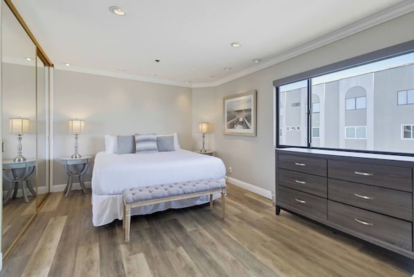 A bedroom with a bed, bedside tables, a dresser, and a large window.