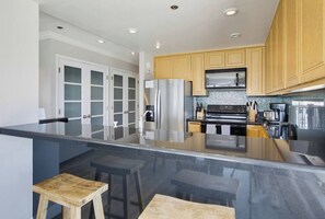 A modern kitchen with a central island, stainless steel appliances, and wooden cabinets. - New photos! Bayfront Penthouse plus parking+bikes! (San Diego)