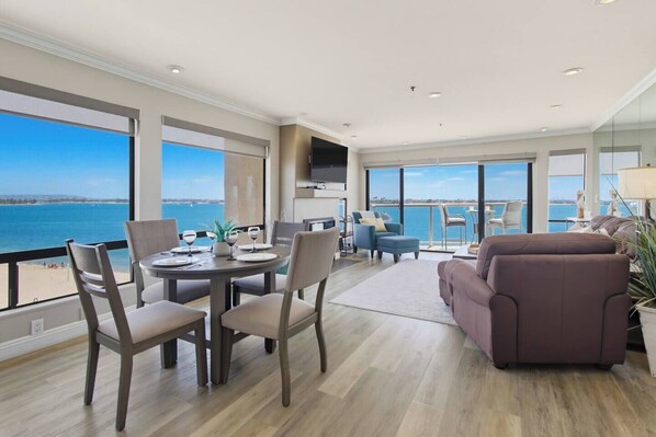 A modern living room with a dining area, large windows, and a view of the sea.