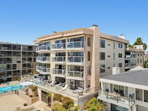 A multi-story residential building with balconies, a swimming pool, and a clear sky.